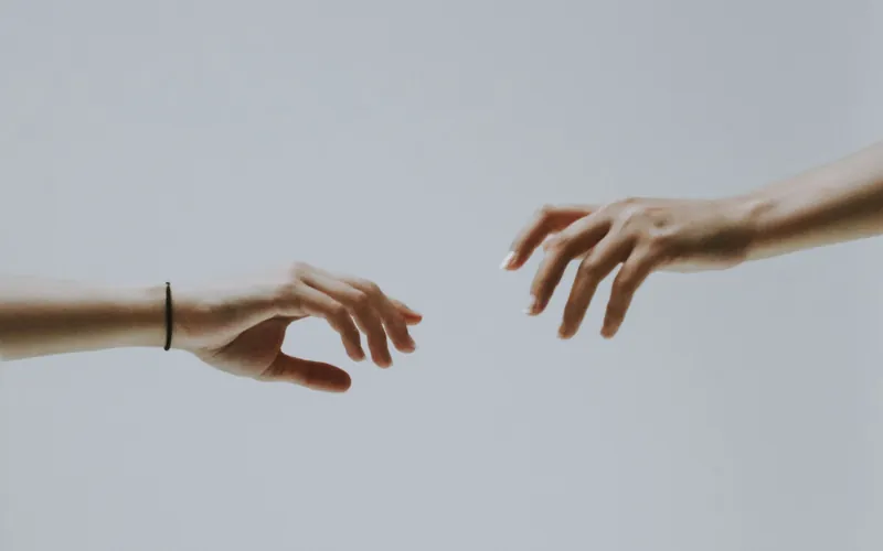 Two hands reaching toward each other against a soft grey background