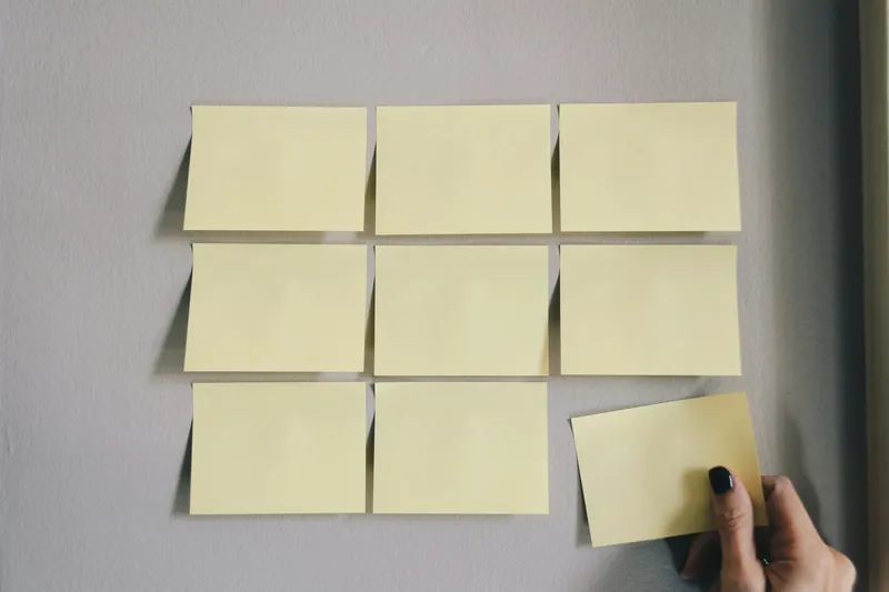 A hand placing the last sticky note in a neat grid on a grey wall